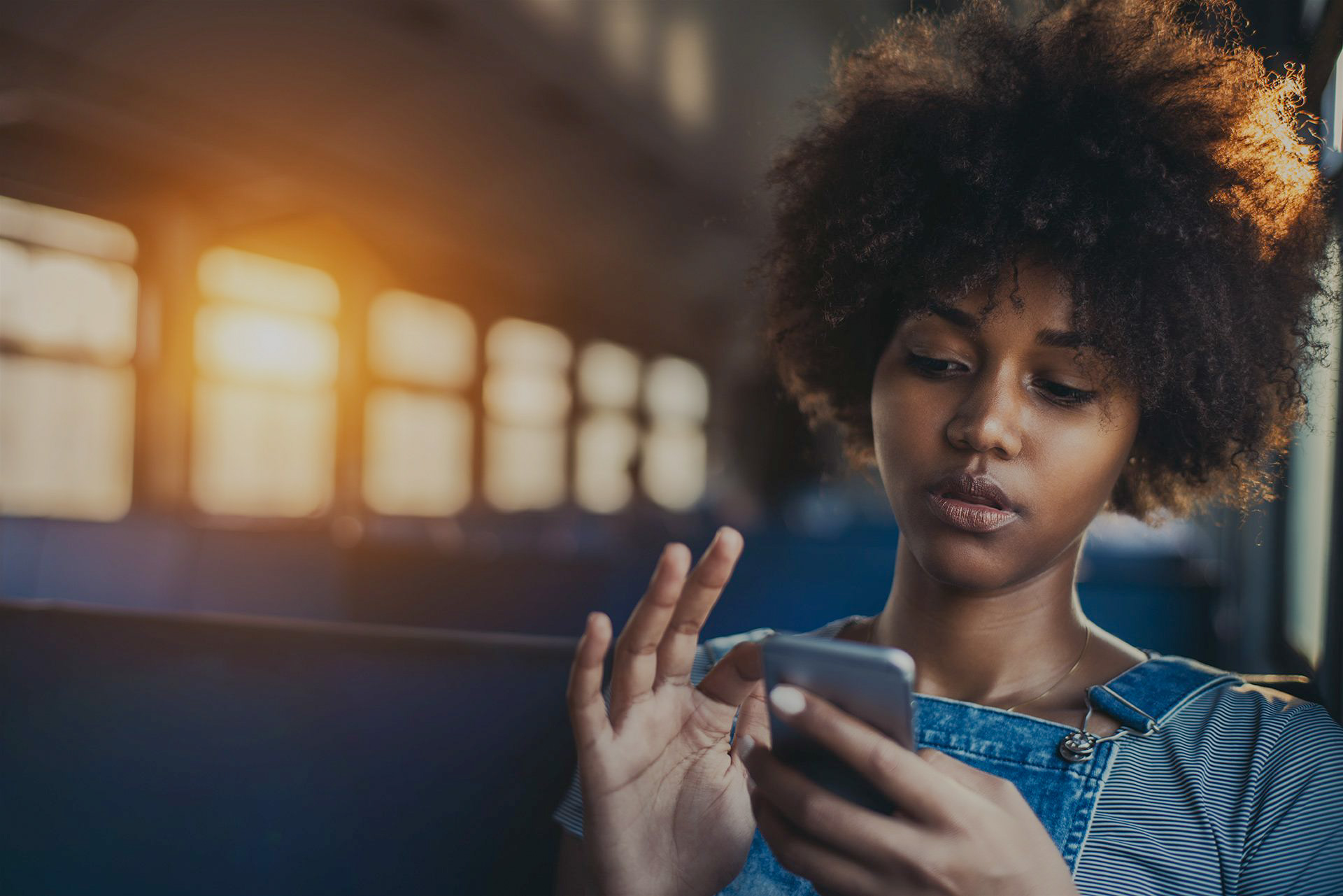 A young woman lit by sunset through train windows, looking with concern at a message on her phone.
